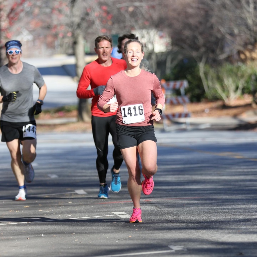 runner, female runner, pink running shoes, pink alphaflys, race day, race day bib, 5k, turkey trot, group of runners
